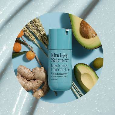 Kind Science Redness Corrector skincare bottle in a light blue color, styled in a flat-lay composition with avocado halves, ginger root, and dried herbs on a textured light blue background.